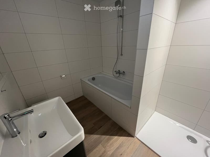 White tiled walls, wooden floor, white bathtub, shower, sink, stainless steel faucet