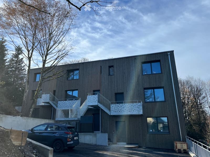 Modern multi-story building, wooden exterior, multiple glass windows, outdoor staircases, car parked in front