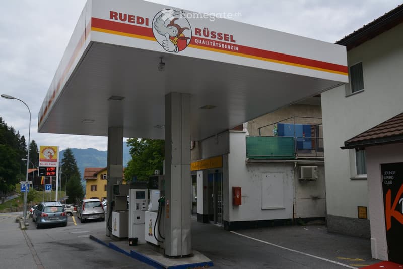 Ruedi gas station, several fuel dispensers, cars, sign board with text and logo