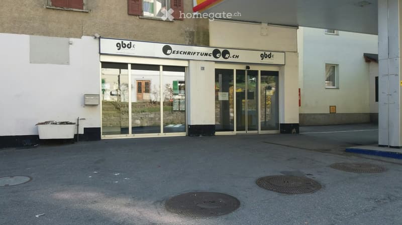 Facade with double doors and windows, entrance with a gas station canopy, three manhole covers