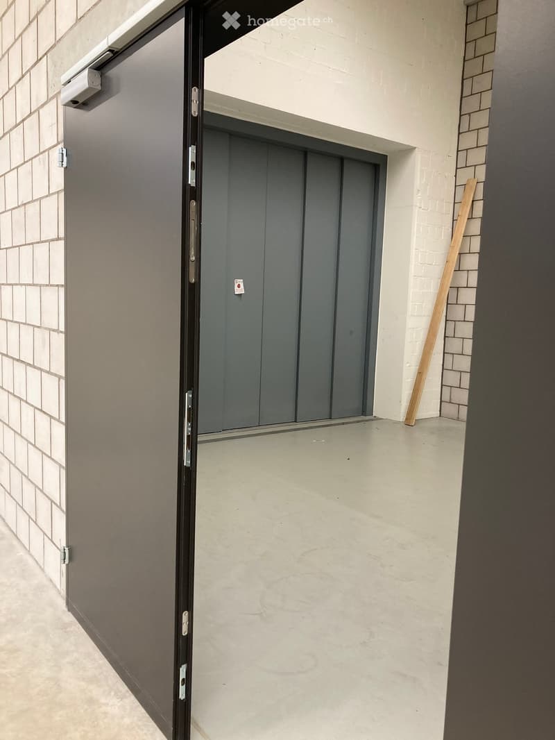 An open door leading to an empty garage with white brick walls and gray doors.