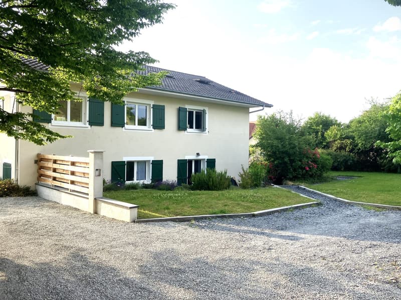 2-story house, green shutters, white walls, gravel driveway, garden with plants and shrubs