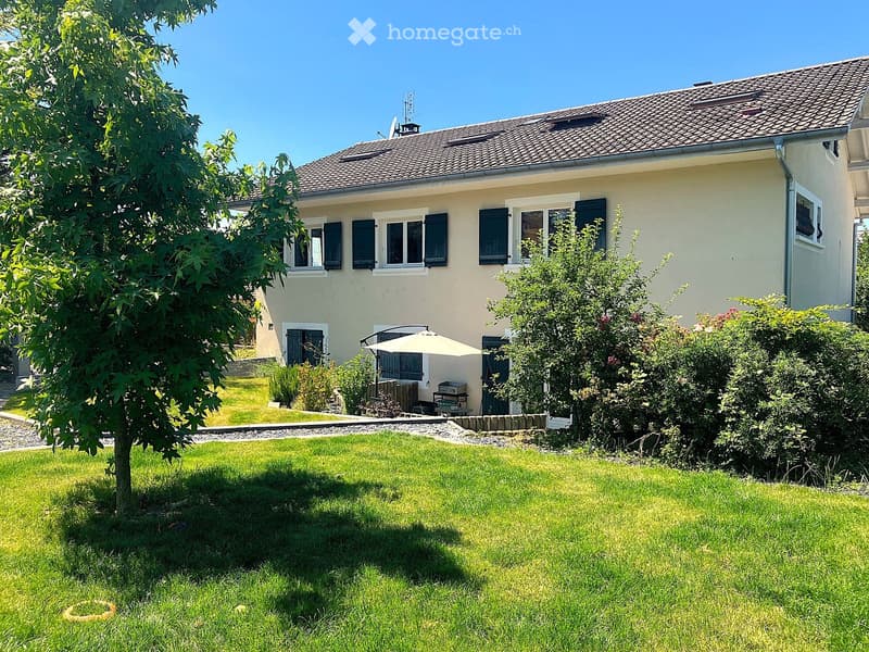 2 story beige house, black shutters, brown roof, tree, barbecue, umbrella, grassy lawn, well kept bushes, plants