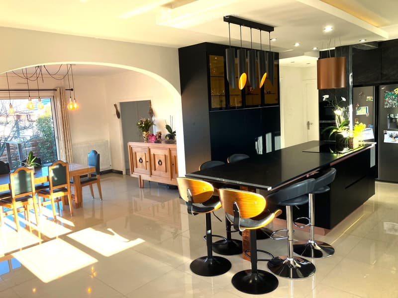 modern kitchen with black counters, wooden chairs and tables, pendant lights, fridge, wooden cabinet, windows