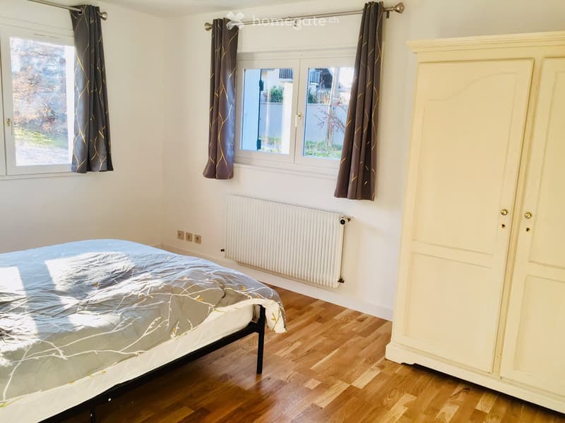 Wooden floor, bed with cover, wardrobe, windows with curtains, radiator