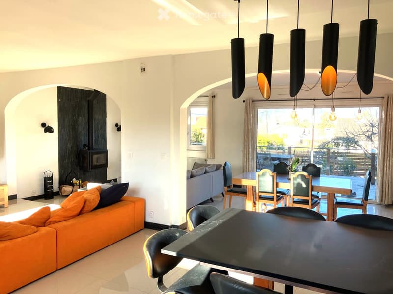 modern living room with orange sofa, dining table with chairs, black lamps, fireplace, glass windows leading to balcony