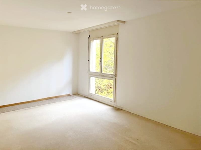 Empty room, white walls, carpeted floor, large window with yellow trees outside