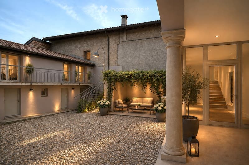 Elegant outdoor patio with a stone-paved floor, a cozy seating area featuring a sofa, coffee table, and chairs, surrounded by potted plants and illuminated by soft lighting.