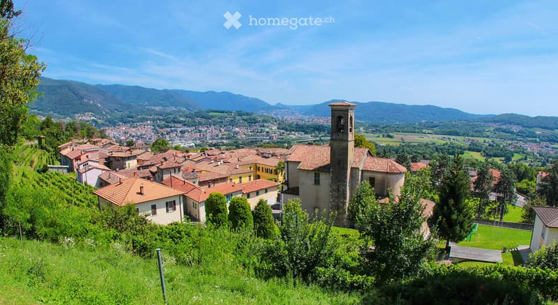 Red tiled roofs, old church tower, green surroundings, hills in the background