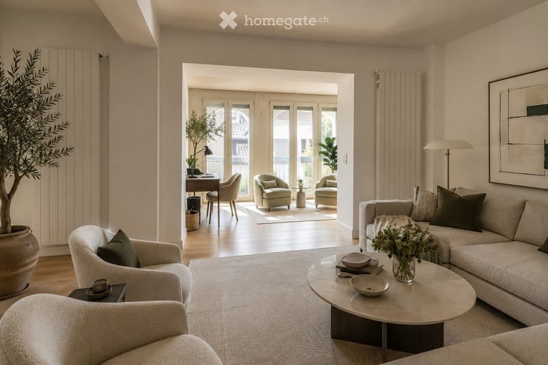 Modern living room with light-colored furniture, including a sofa, armchairs, coffee table, and a desk area with a chair. The space features large windows and a view of a balcony, with decorative elements like a floor lamp, picture frame, and vase on the