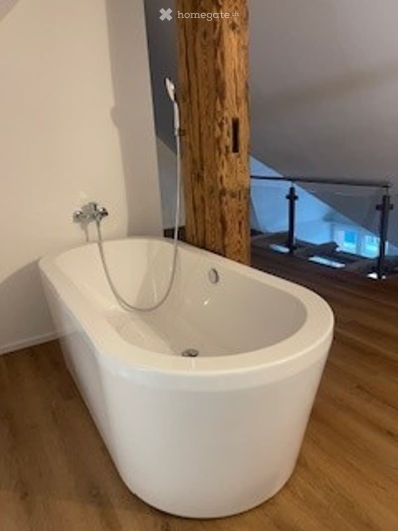 white freestanding bathtub, shower head, wooden floor, white wall