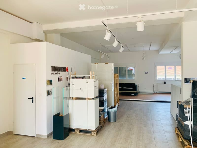 large room, high ceiling, tiled floor, multiple lamps, white cabinets, trash bin, open doorway