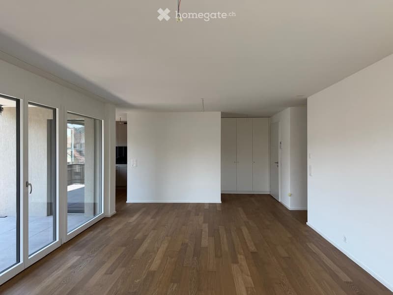 Empty room with wooden flooring, white walls, large glass sliding doors leading to a balcony, and a closet in the background.