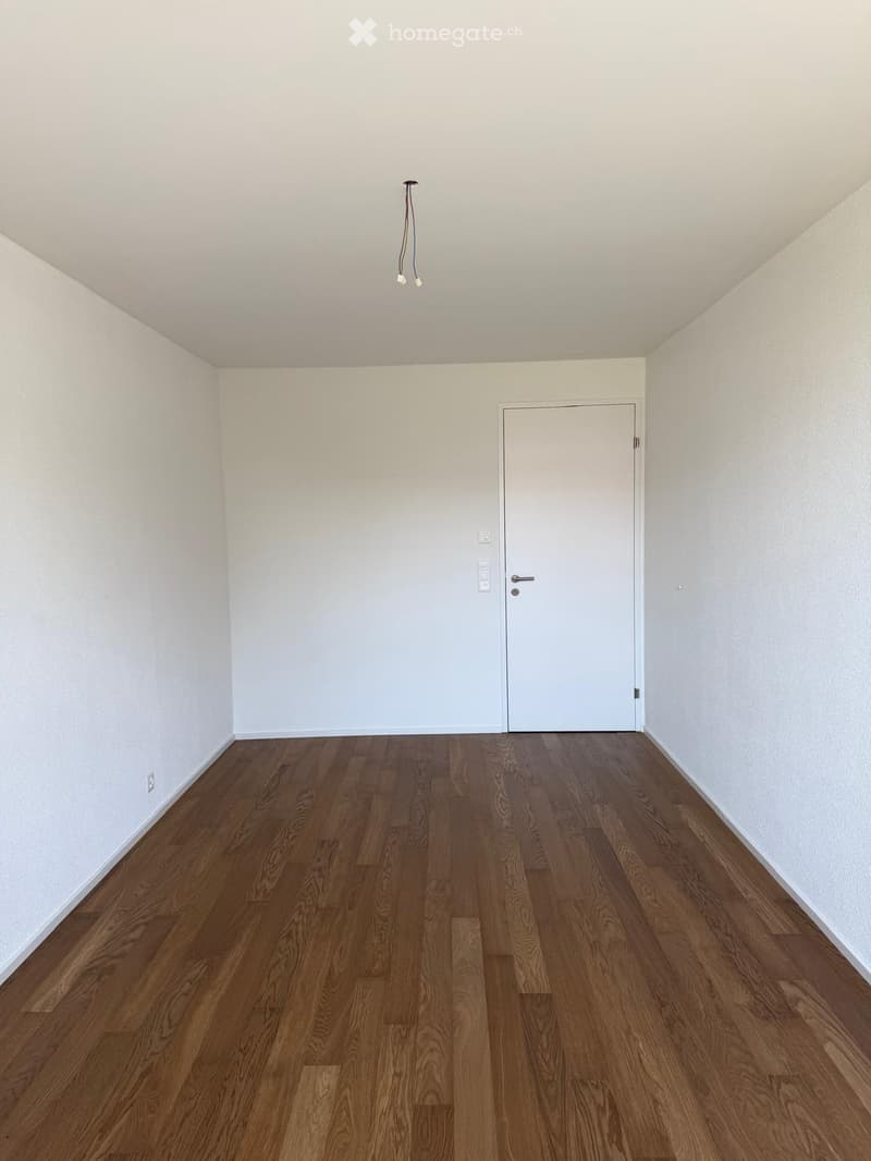 Empty room with wooden flooring, white walls, and a single door.