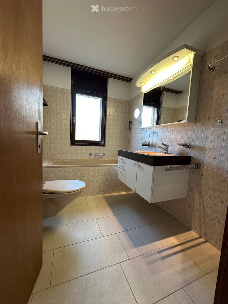 Modern bathroom with bathtub, sink, and toilet, a vanity with cabinet, and a mirror with lights