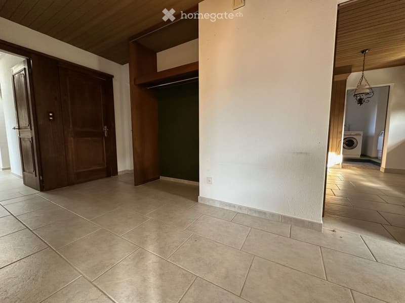 Empty room with tiled floor, wooden ceiling, wooden closets, and a washing machine in a side room.