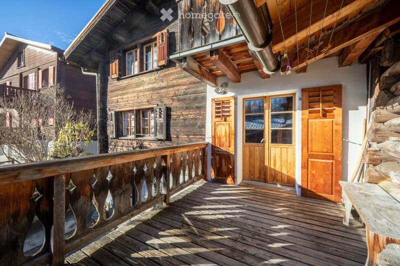 Timber building, 2nd story balcony, large front porch with wooden railing, two large doors, stone log stack