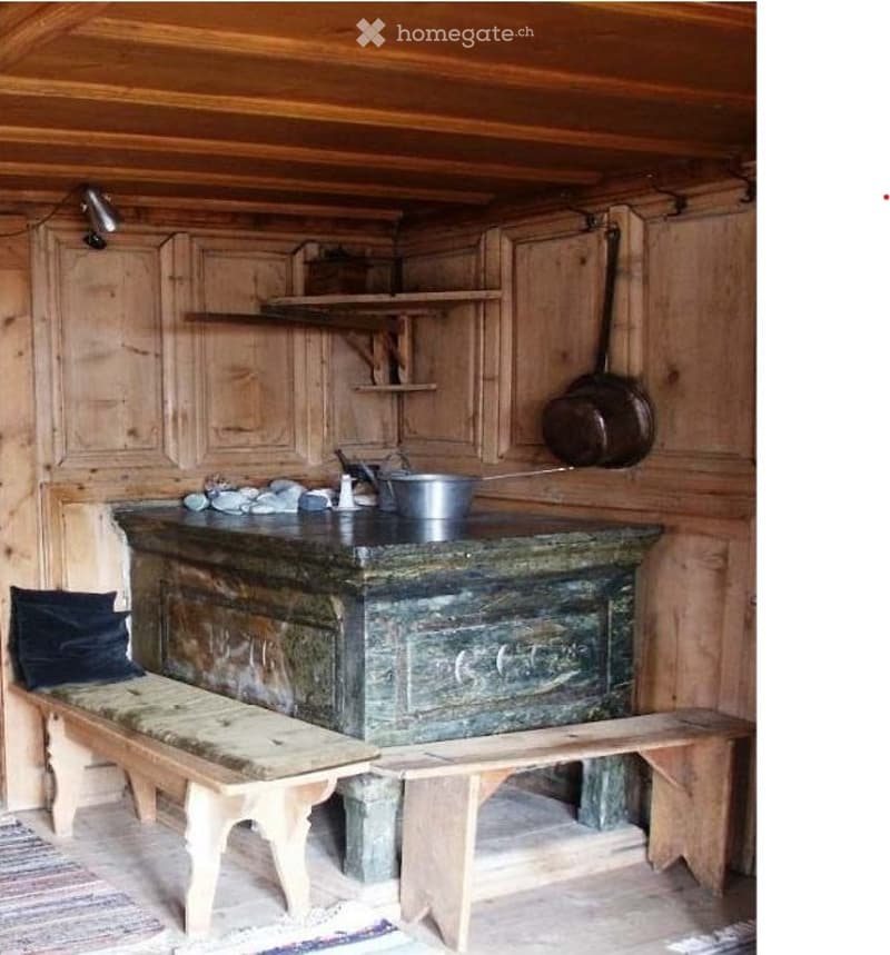A room with wooden walls and a wooden bench, two pots hanging on the wall, a green table and a bucket on top