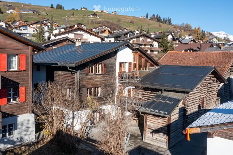 wooden log chalets, mountain slope in the background, solar panels on roofs, red shutters
