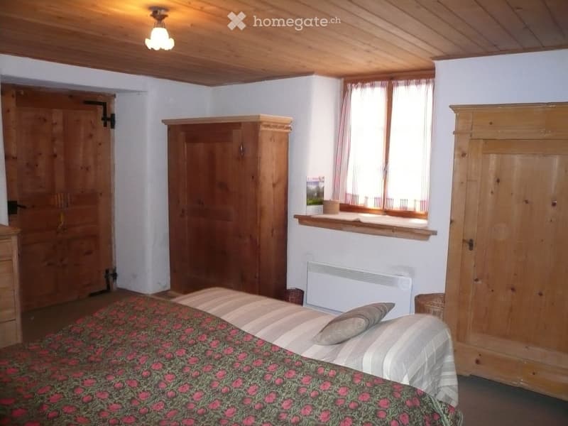 Bedroom with bed, wooden wardrobes, a window with curtains, radiator, and a wooden cabinet with a pot on the window sill