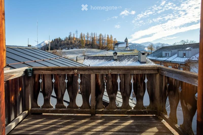 View of snowy mountains, wooden railings, mountains in the background, and buildings in the foreground