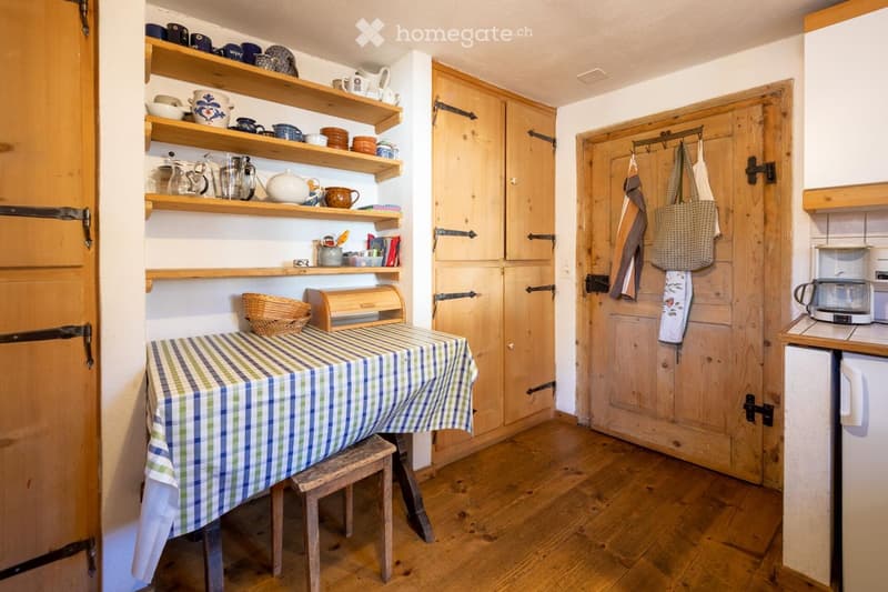 Wooden floor, checkered tablecloth, shelves with cups and teapots, wooden doors, coffee maker