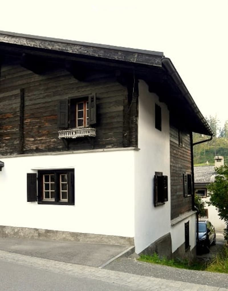 Alpine style wooden house, two story, wooden wall, white painted lower wall, black wooden windows and shutters, metal gutter