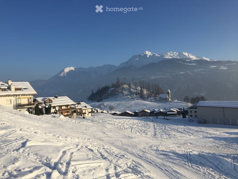 Aerial view of snowy mountains, village, several houses, ski slopes, clear blue sky