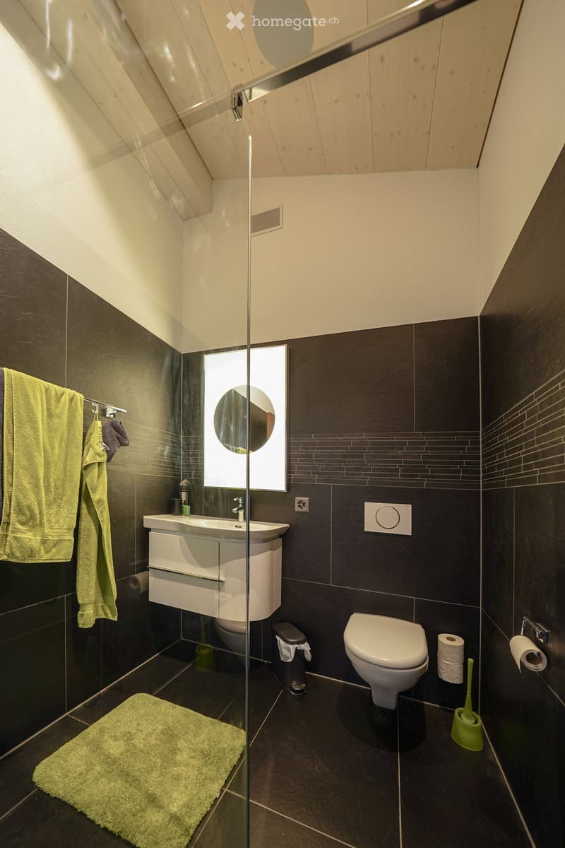 modern bathroom with white sink, green rug, dark walls, white toilet, shower, green towel, mirror