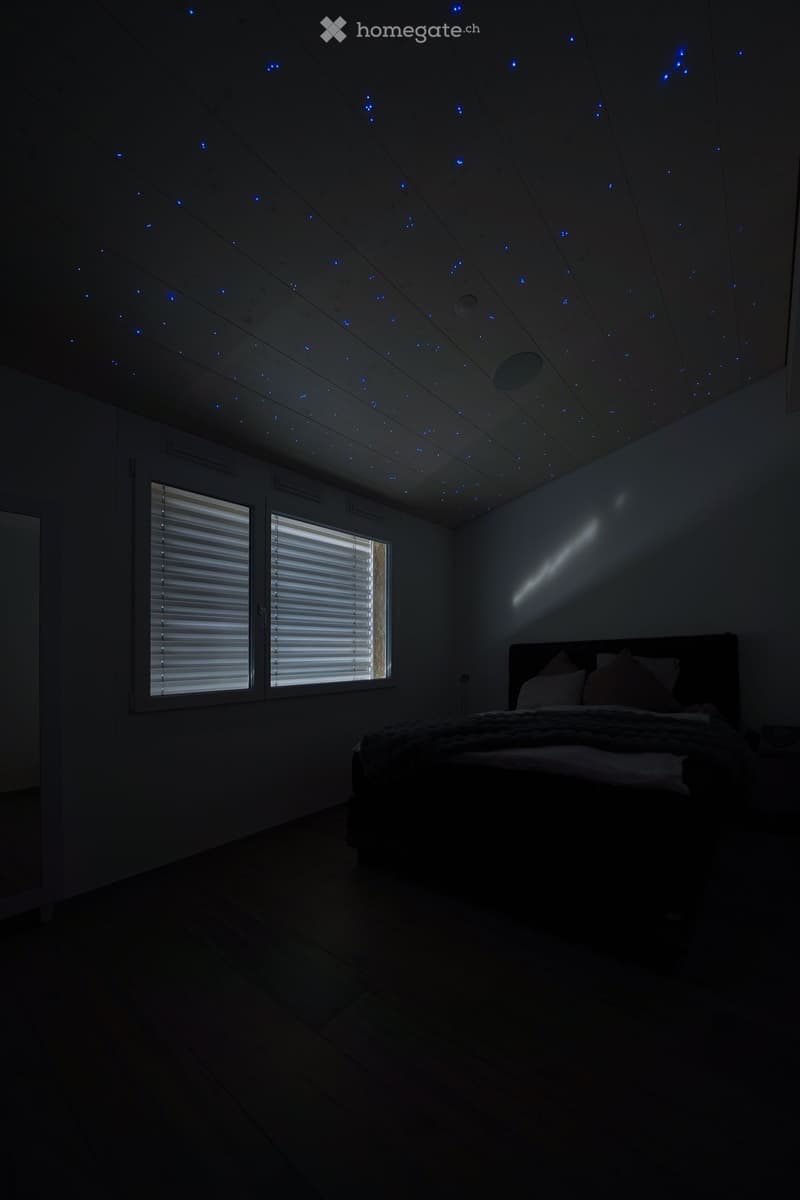 Bedroom with star-like lights on the ceiling, bed with pillows, and two windows with white blinds
