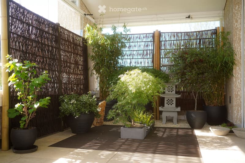 outdoor covered area with several potted plants, bamboo fence, and decorative stone lantern