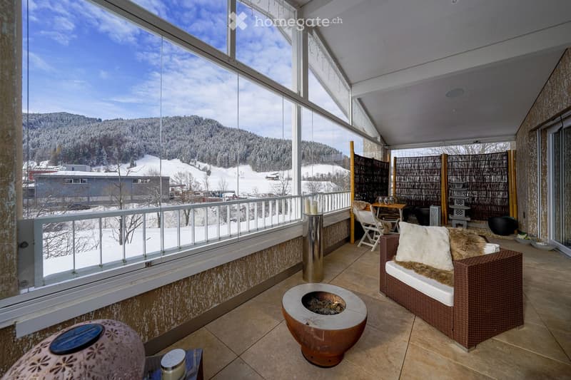 A large terrace with full glass walls offering a snowy view, a fire pit, sofa, and a table.