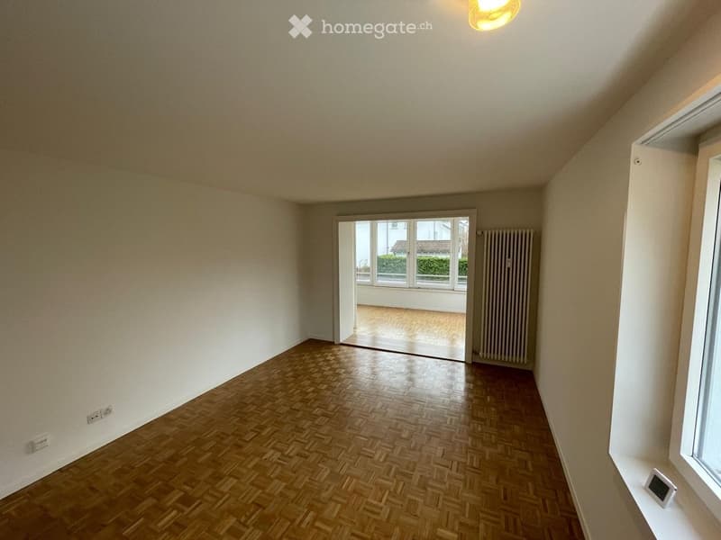 empty room with white walls, wooden parquet flooring, a white radiator on the wall, sliding doors to a balcony, large window with a view