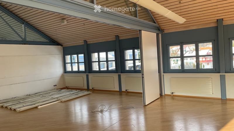 large room with wooden floor, white walls, windows, wall-mounted radiators, open door