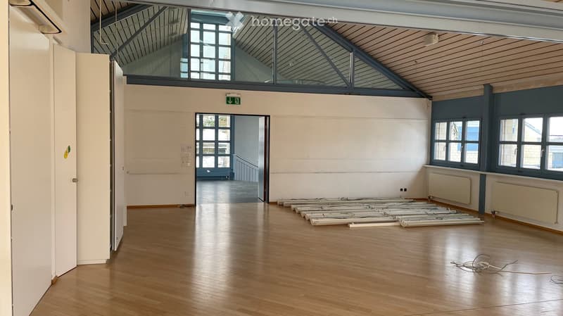 open room with no furniture, wooden floor, white walls, open door, glass windows, emergency exit sign
