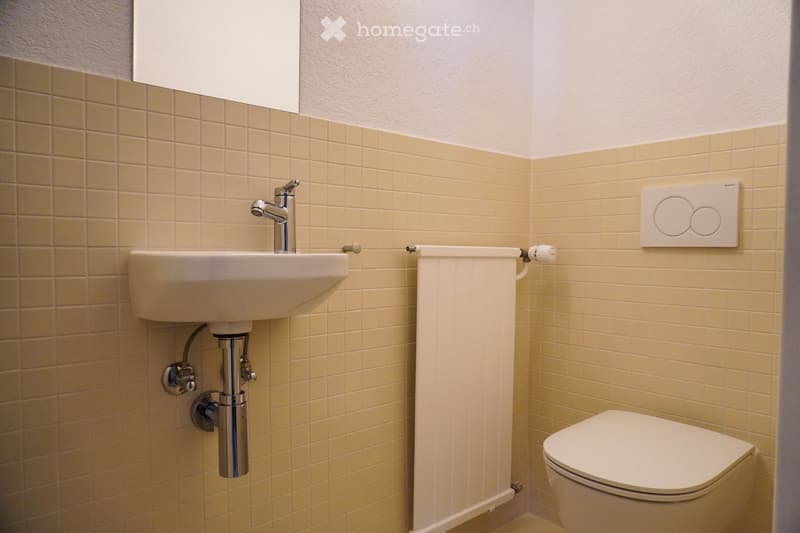 Bathroom with beige tiles, white sink, toilet, white radiator, faucet, mirror