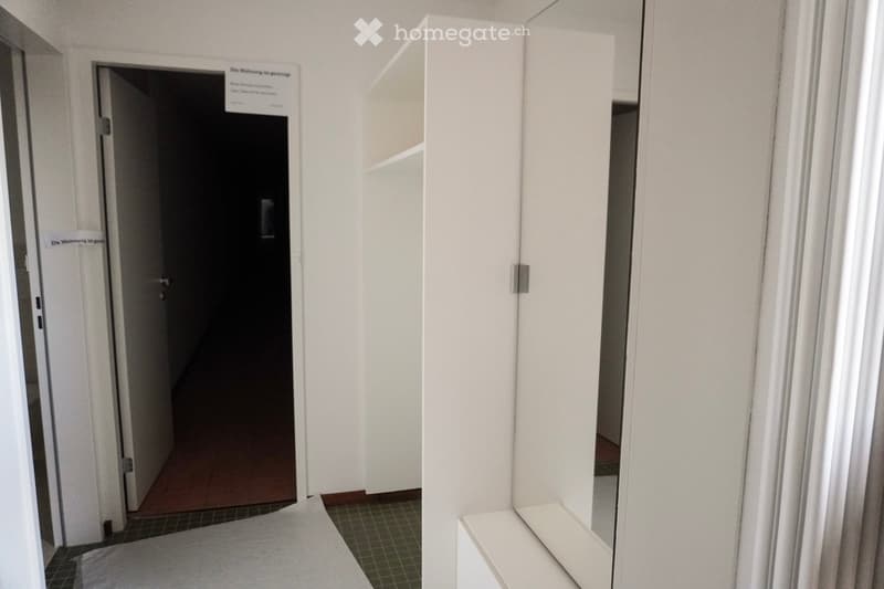 corridor with open door, hallway with tile floor, white walls, mirror