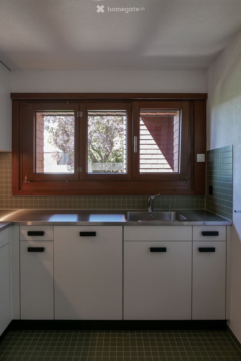 Modern kitchen with stainless steel sink, white cabinets, and large windows overlooking a garden.