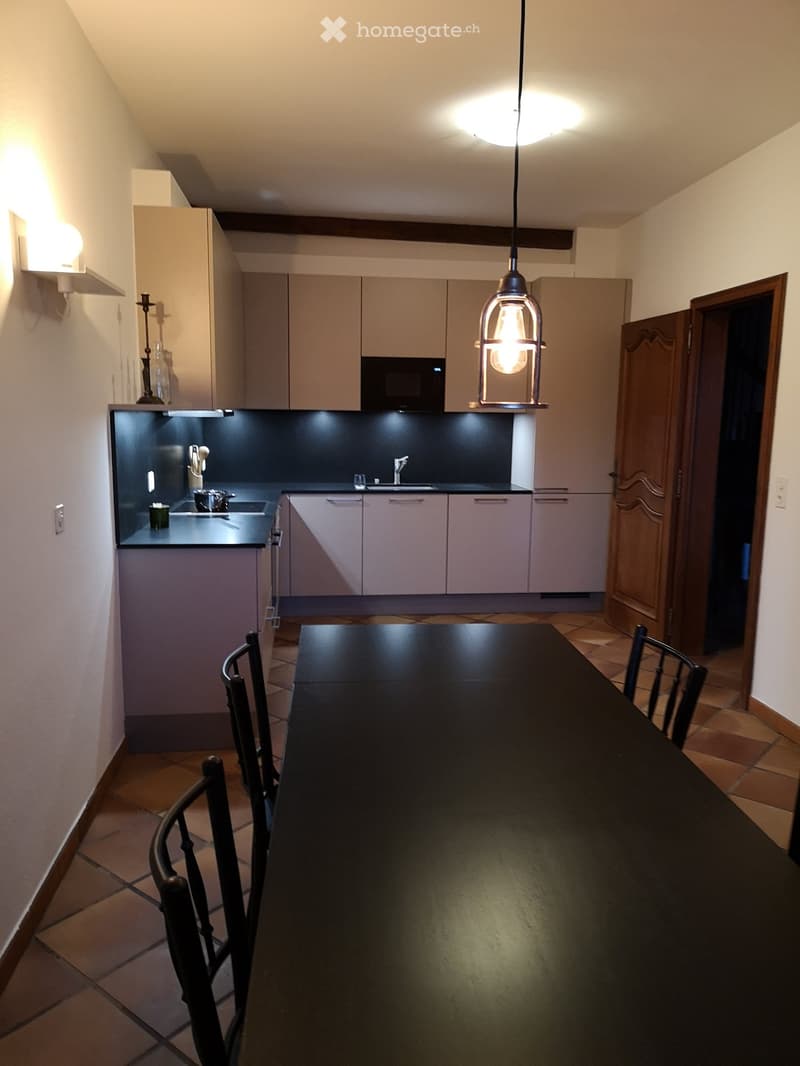 modern open plan kitchen with dining table, black countertop, kitchen island with sink, hanging lamp, microwave, drawers and cabinets, power outlets