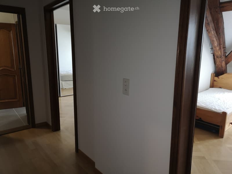 bedroom with a bed, wood beams on the ceiling, open door to another room, wooden floors