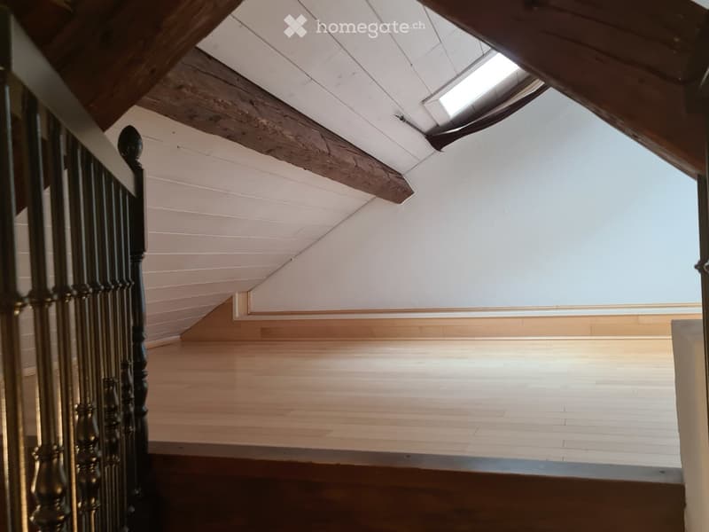 empty attic with hardwood flooring and wooden beams on the ceiling