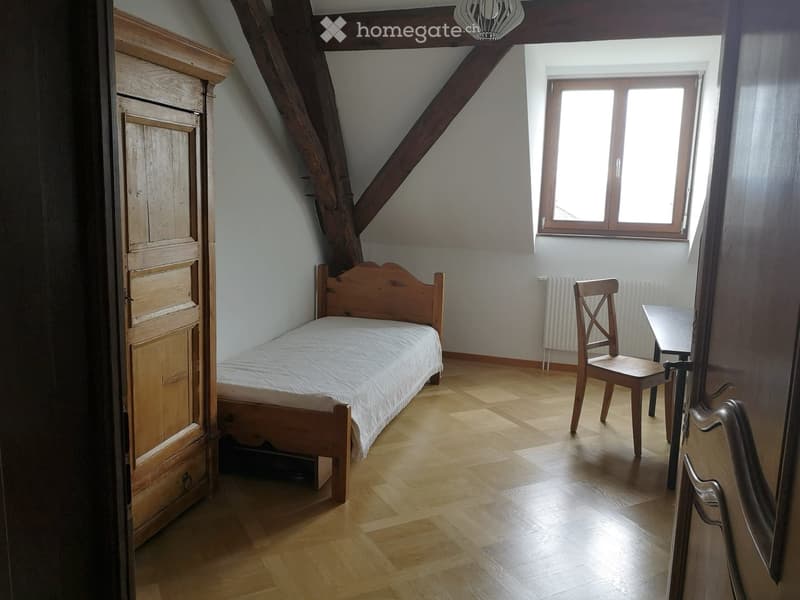 room with bed, wooden cabinet, chair, small table, window, wooden ceiling beams