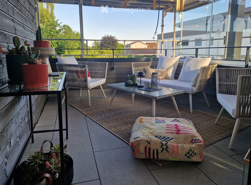 Balcony with a sofa, chairs, a coffee table, a colorful pouf, and potted plants.