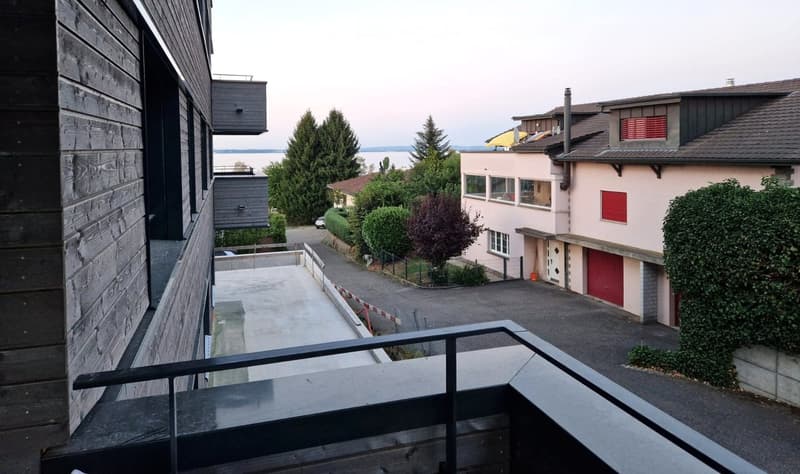 Balcony overlooking a residential area with a view of neighboring houses, trees, and a body of water in the distance.