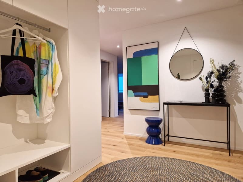 Modern hallway with a white bench, a black console table, a blue stool, a round mirror, and a colorful abstract artwork on the wall.