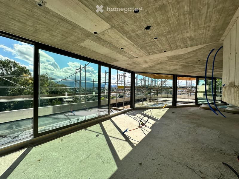 An unfinished room with large windows, concrete walls and floors, and scaffolding outside
