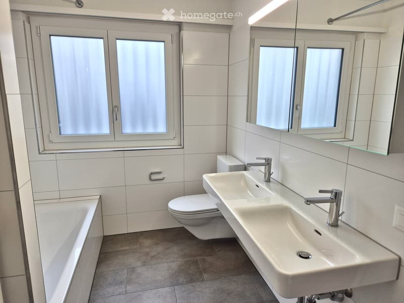 Bathroom with a bathtub, two sinks, and a toilet; tiled walls and floors; mirror