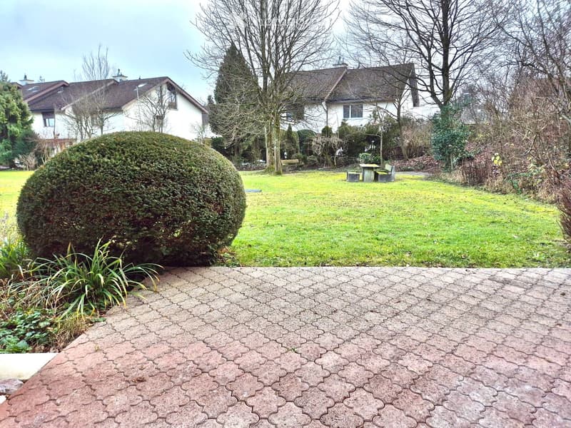 paved garden path, neatly trimmed hedges, lawn, grassy area, pathway leading to the house, seating area with a table and benches, and trees