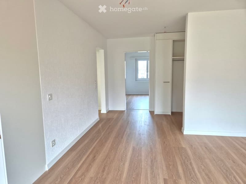 empty room, wooden floor, white walls, 2 doors, window at the end of the hallway