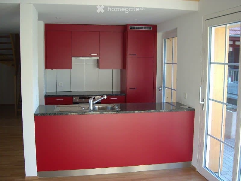 modern kitchen with red cabinets, a granite countertop, a sink with a faucet, a glass door, and wooden flooring